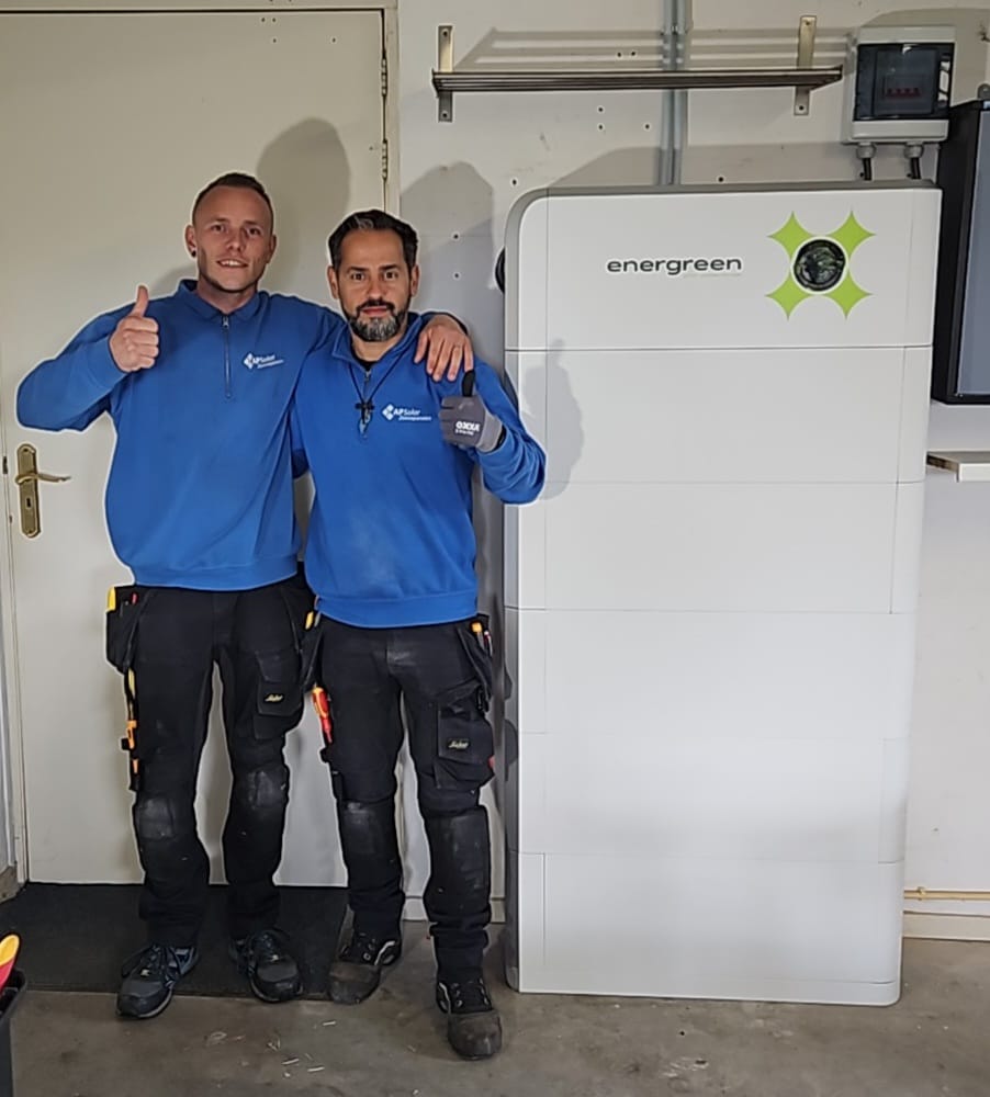 Twee installateurs van APSolar poseren voor de foto naast een 48 kWh Energreen Power Store thuisbatterij voor zonnepanelen